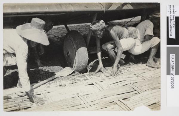 Local villagers lay panels from their bamboo huts underneath the bogged wheels of the Vickers Vimy aircraft in Surabaya, Indonesia, 1919