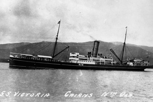 Large ship sailing past mountain range in the background.